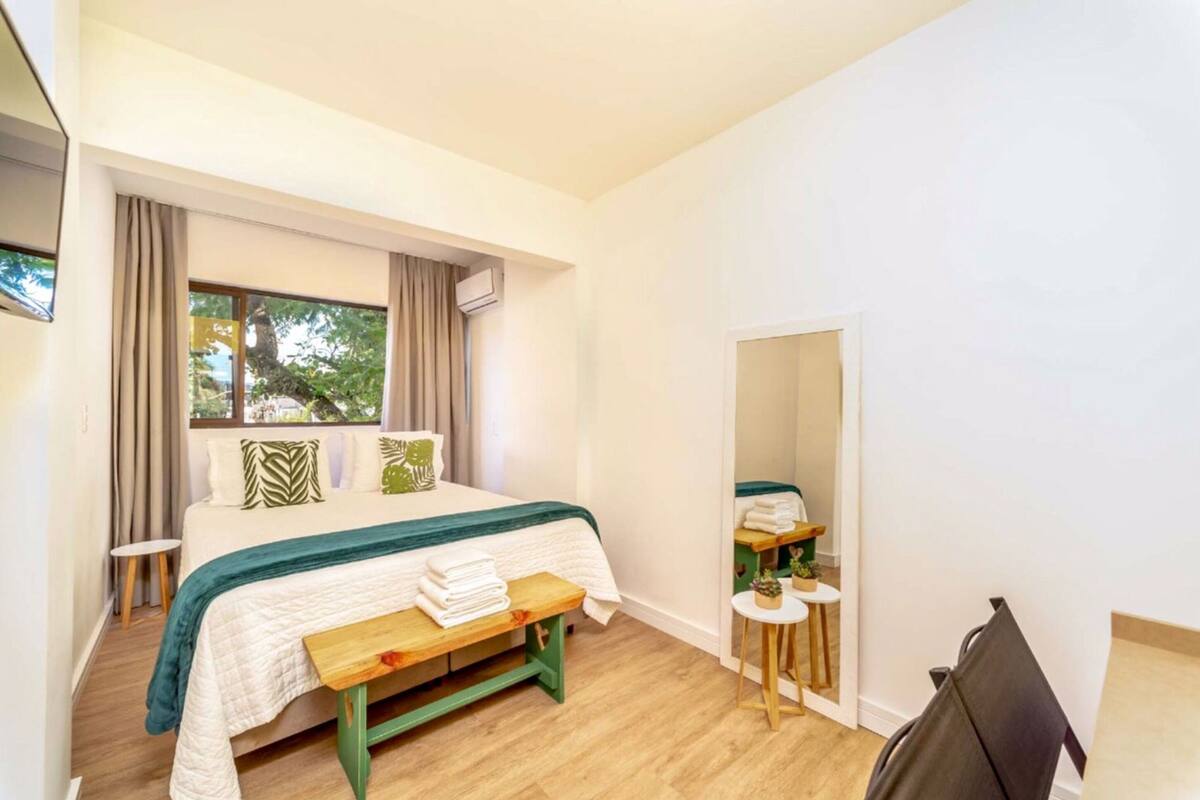 A bedroom with a bed, a bench, a small table, and a mirror.