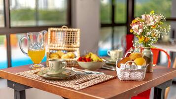 A breakfast table with a pitcher of orange juice, a cup, a basket of bread, a bowl of fruit, and a vase of flowers.