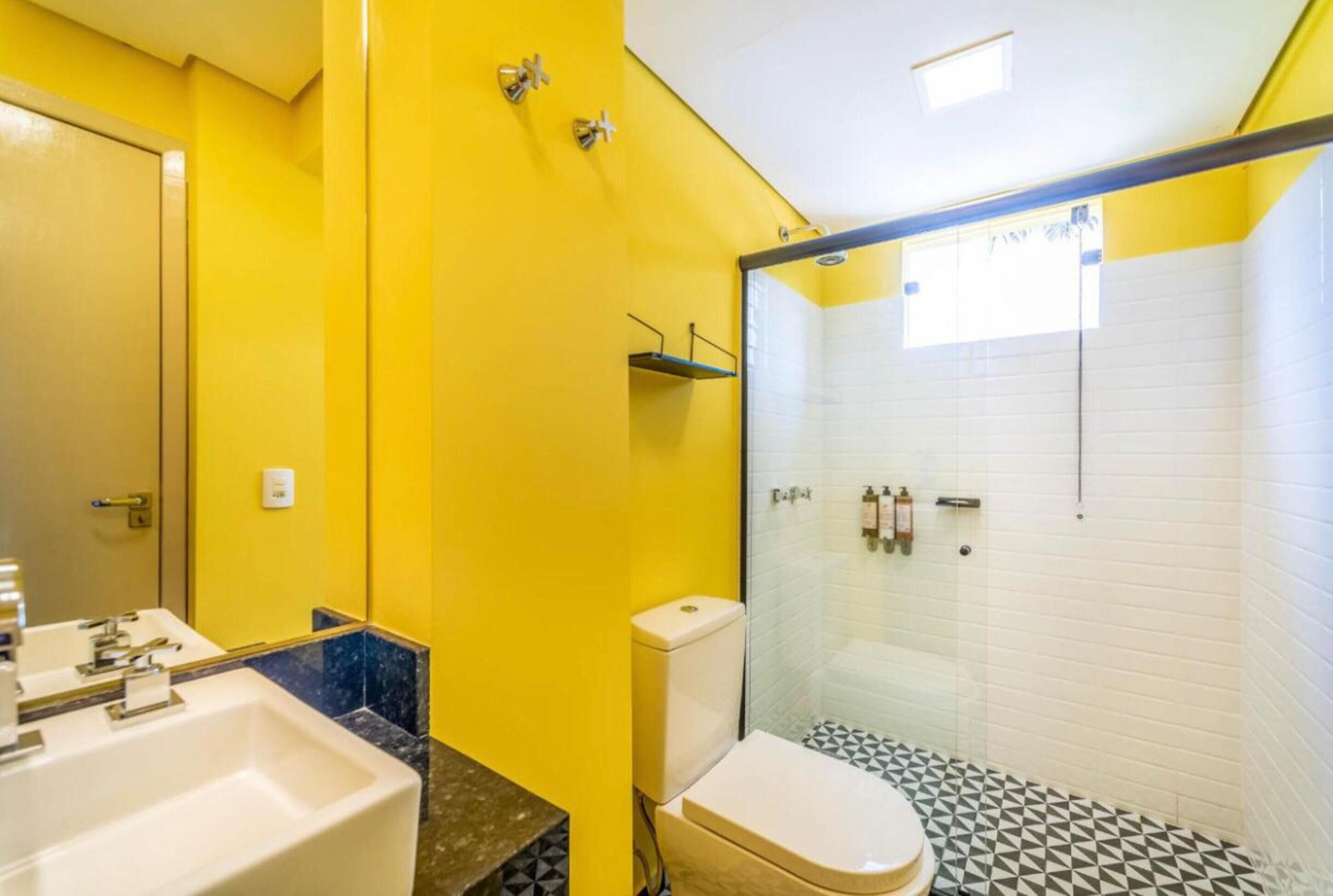A bathroom with a yellow wall, a white sink, a toilet, and a glass-enclosed shower area.