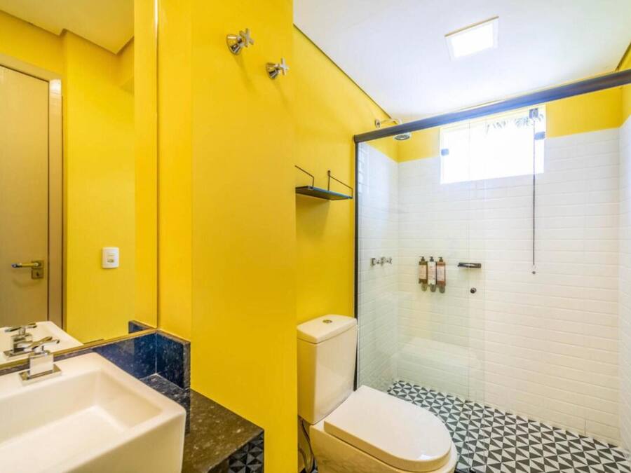 A bathroom with a yellow wall, a white sink, a toilet, and a glass-enclosed shower area.