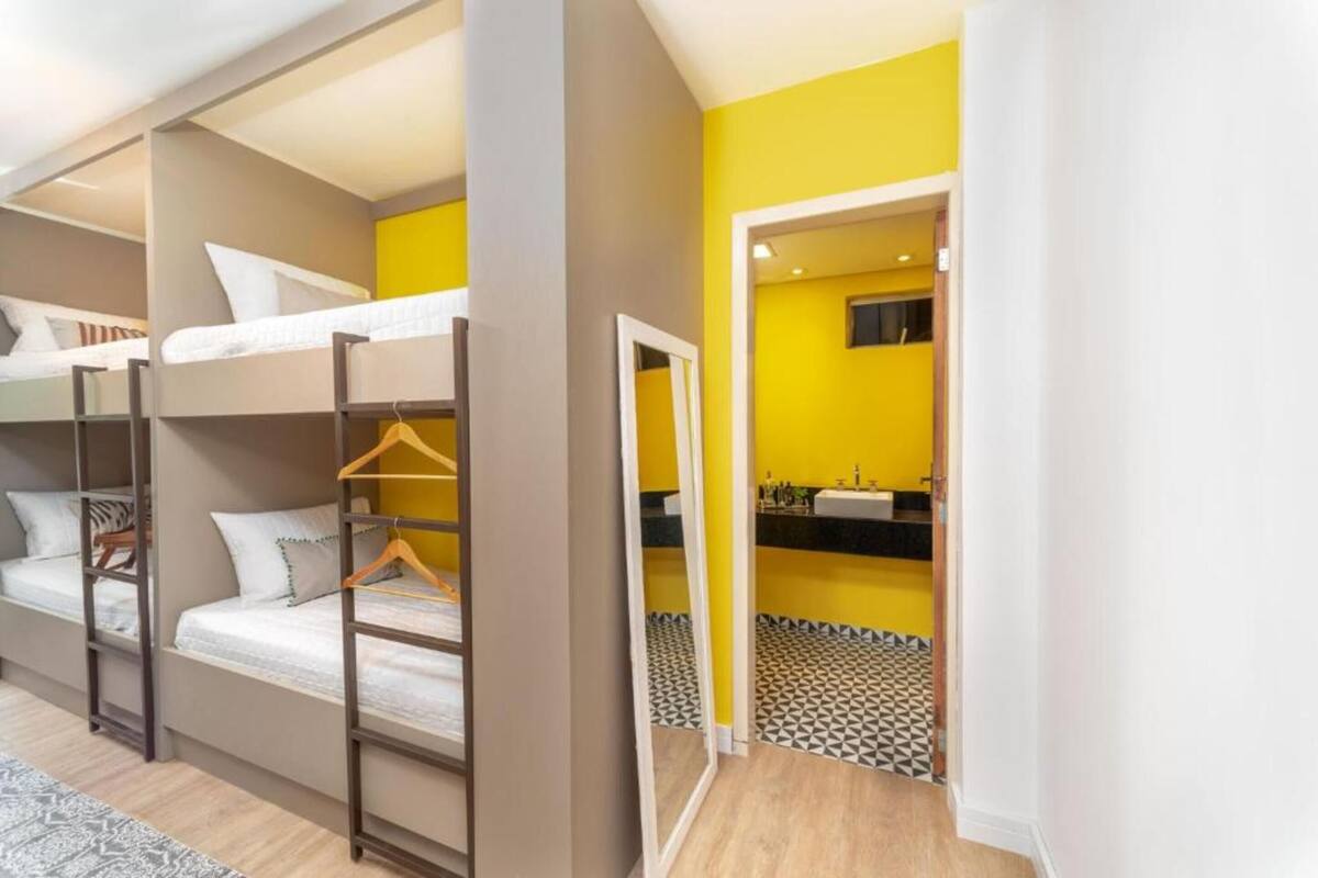 A room with bunk beds, a mirror, and a bathroom with a sink and mirror.
