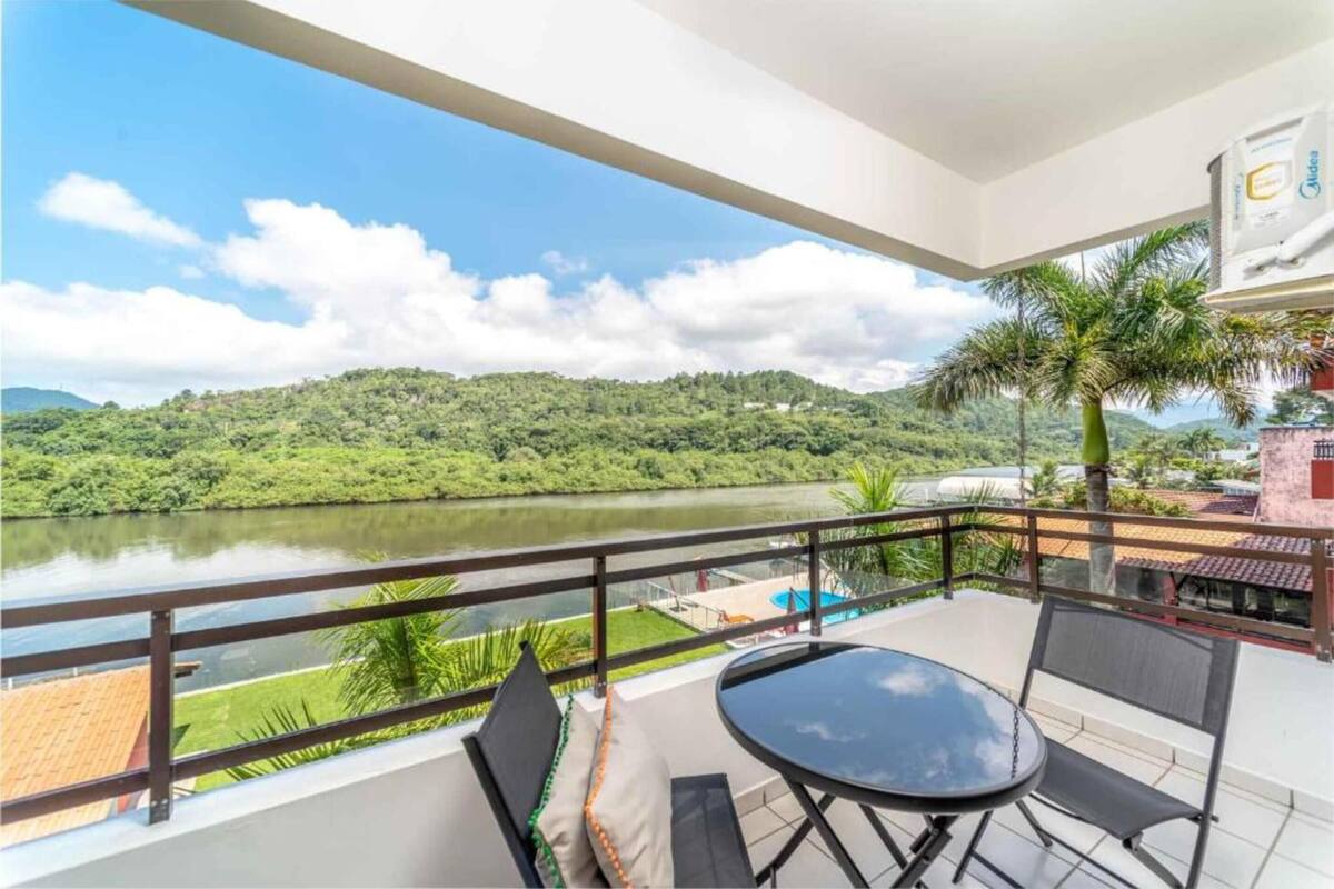 A balcony with a view of a river and hills, a table and chairs, and a palm tree.