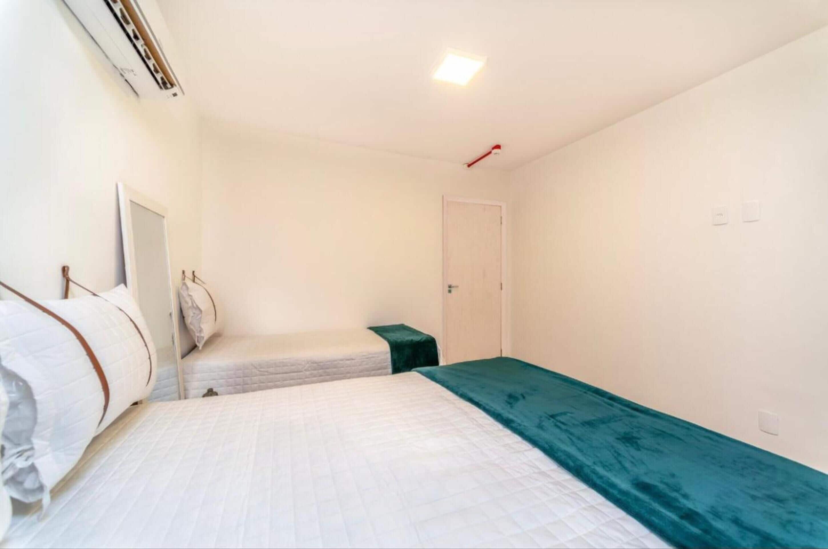 A single bedroom with a bed, a small bedside table, a door, and a wall-mounted air conditioning unit.