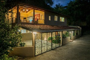 Une maison à deux étages dotée d’un balcon, d’un patio agrémenté de plantes et dont l’intérieur est visible, notamment la salle à manger.