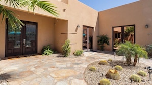 A courtyard with a stone pathway, palm trees, and cacti.