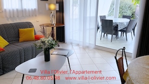A modern living room with a sofa, coffee table, and a dining area with chairs and a table. - Gîte Villa l'Olivier - charm, tranquility, beach at VAUX SUR MER / ROYAN. (VAUX SUR MER)
