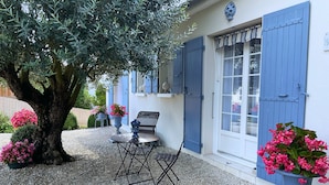 A patio with a table and chairs, a large tree, and potted plants. - Gîte Villa l'Olivier - charm, tranquility, beach at VAUX SUR MER / ROYAN. (VAUX SUR MER)