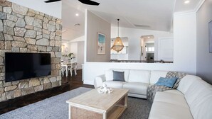 A modern living room with a stone accent wall, a flat-screen TV, a white sofa, and a wooden coffee table. - Hamptons Ocean Escape - The most beautiful home for your next luxurious, relaxing getaway (Ulladulla)