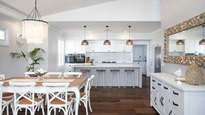 A modern kitchen with white cabinetry, a central island, pendant lights, and a large mirror above the island. - Hamptons Ocean Escape - The most beautiful home for your next luxurious, relaxing getaway (Ulladulla)