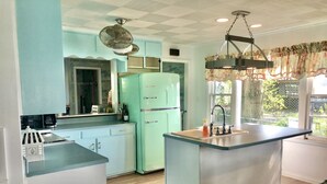 A kitchen with a central island, a vintage-style refrigerator, and a window with a view of greenery.