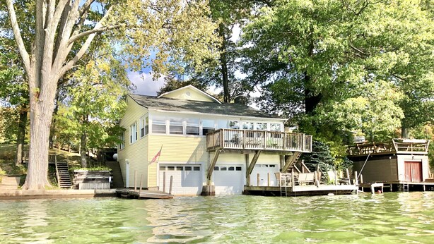 A house with a dock extending into a greenish water body, surrounded by trees.