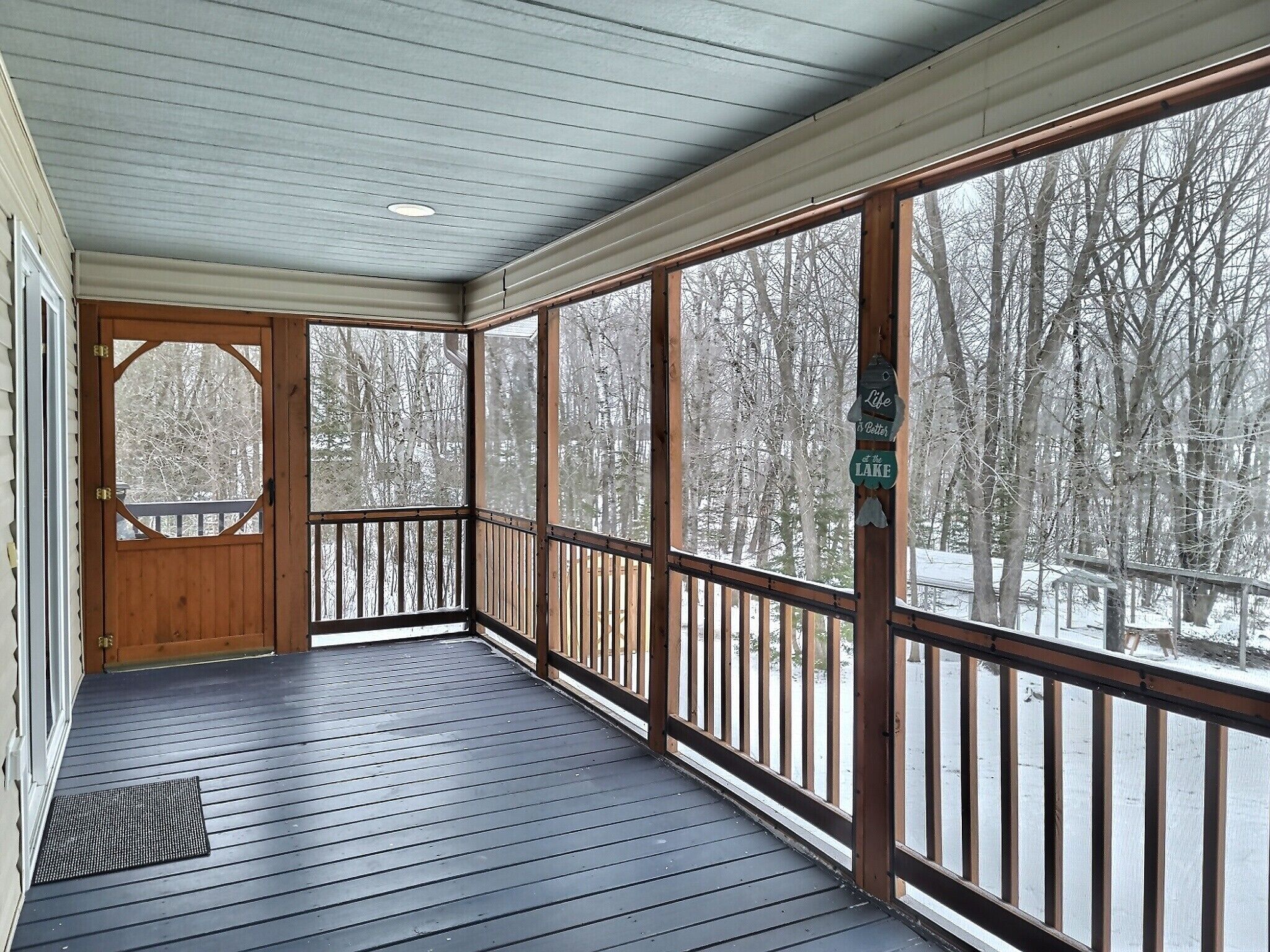 A covered porch with a wooden railing, a door with a window, and a view of a snowy landscape.