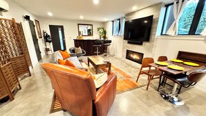 A modern living room with a sofa, coffee table, and dining table. There is a fireplace, a TV mounted on the wall, and a window with curtains. - Restful, Convenient Getaway Near Downtown and Seattle’s Largest Park (Seattle)