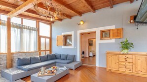 Un salon chaleureux avec un canapé d’angle, un plancher en bois et un coin repas où se trouve un plateau de nourriture.