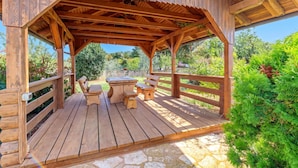Une terrasse en bois agrémentée d’une pergola, d’un revêtement de sol en pierre et d’une petite table avec des bancs.