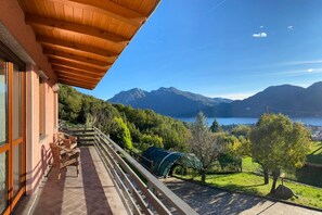 A balcony with wicker furniture, a wooden ceiling, and a view of mountains and a lake.