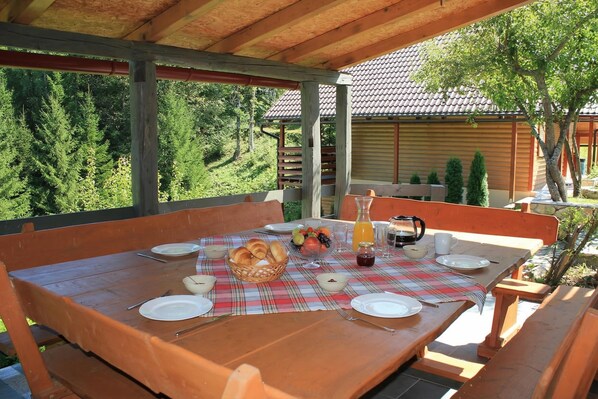 A wooden table set for breakfast with a plaid tablecloth, plates, cutlery, a fruit bowl, and a pitcher of juice. - Chalet Zavrh with Private Heated Pool (Brod Moravice)
