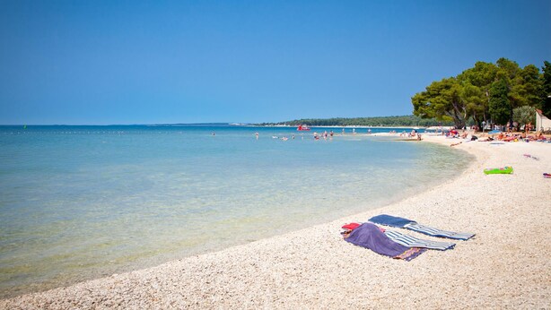 A beach with clear water, pebbles, and umbrellas. - Pool & Spa House Betiga 2 (Vodnjan)