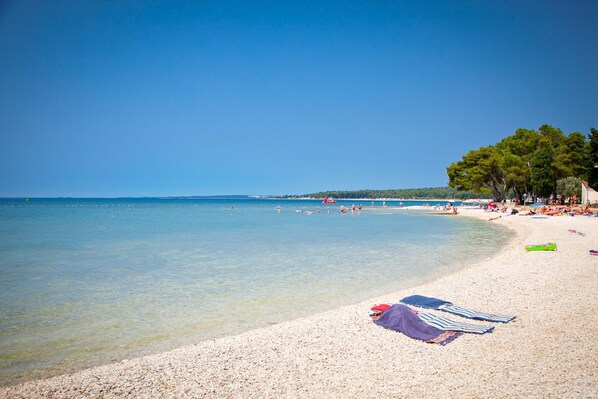 A beach with clear water, pebbles, and umbrellas. - Pool & Spa House Betiga 2 (Vodnjan)