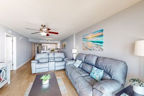 A modern living room with a grey leather sofa, a coffee table with a plant, and a ceiling fan.