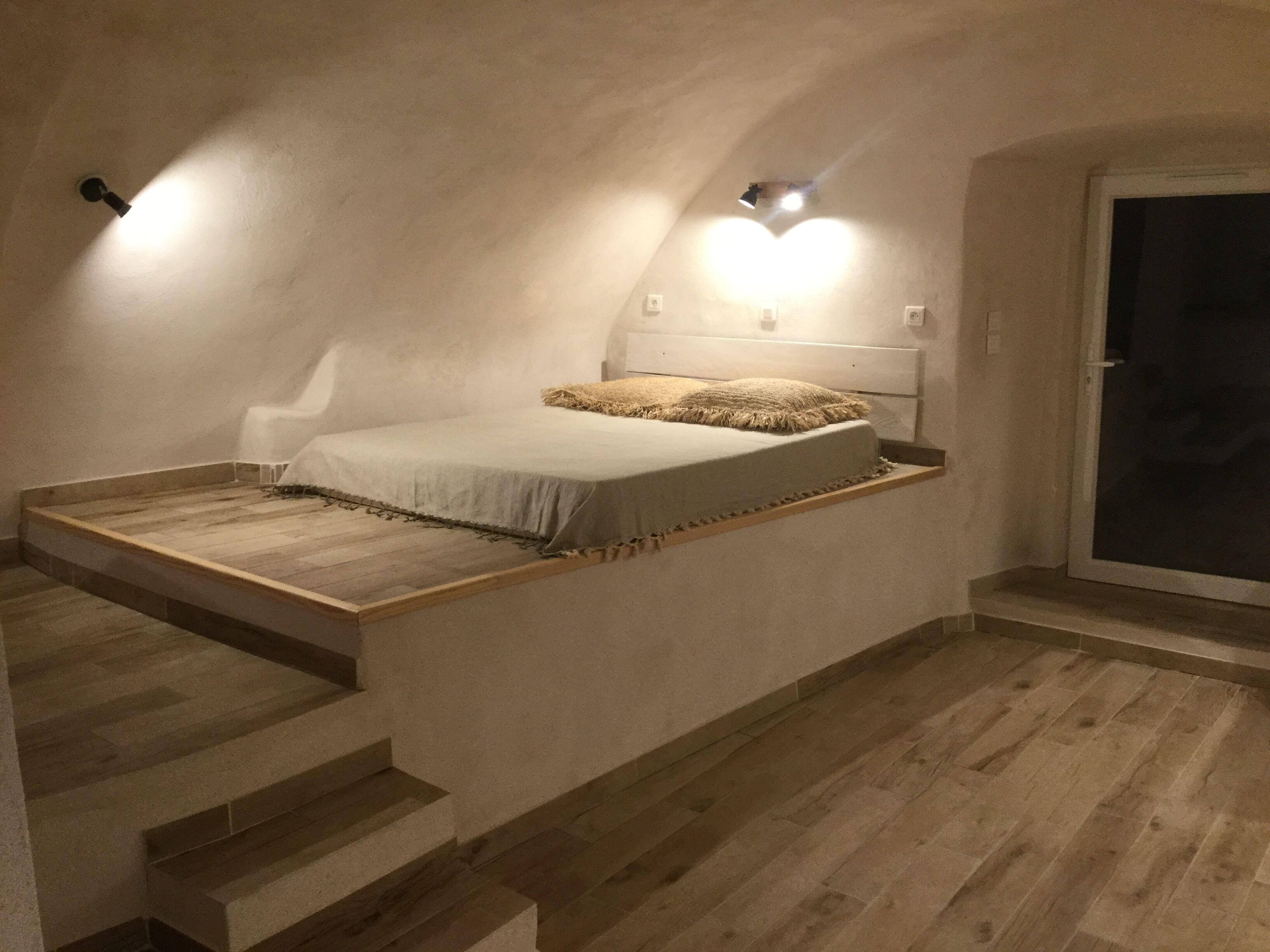 A bedroom with a sloped ceiling, a bed with a white mattress and a beige throw, and a wooden floor.