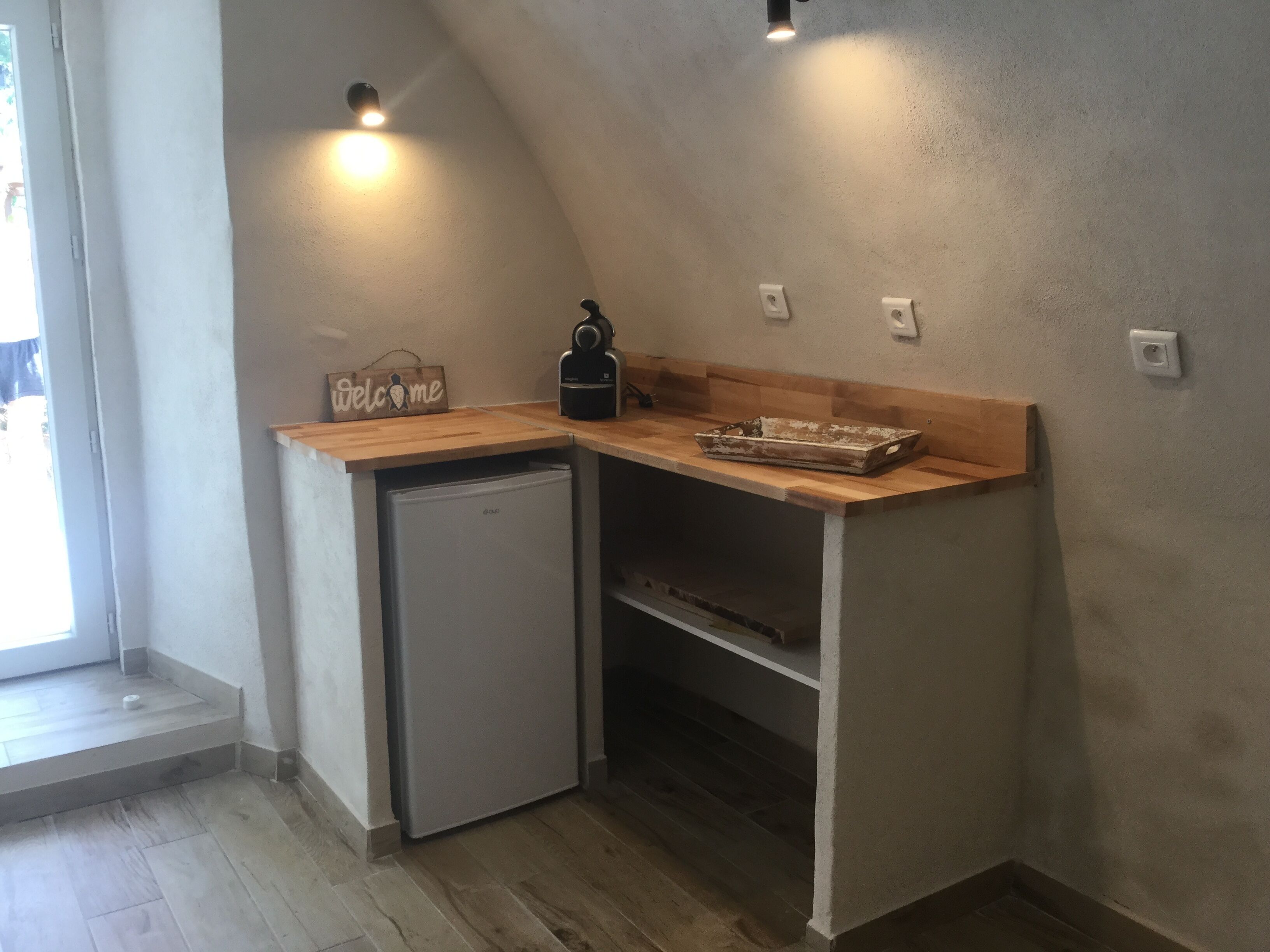 Una cocina compacta con refrigerador integrado, una encimera de madera y un cartel que dice 'Welcome'.