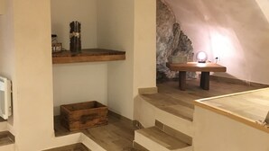 Una scala in legno conduce a una zona mansardata con una parete in pietra e un piccolo tavolo con una luce.