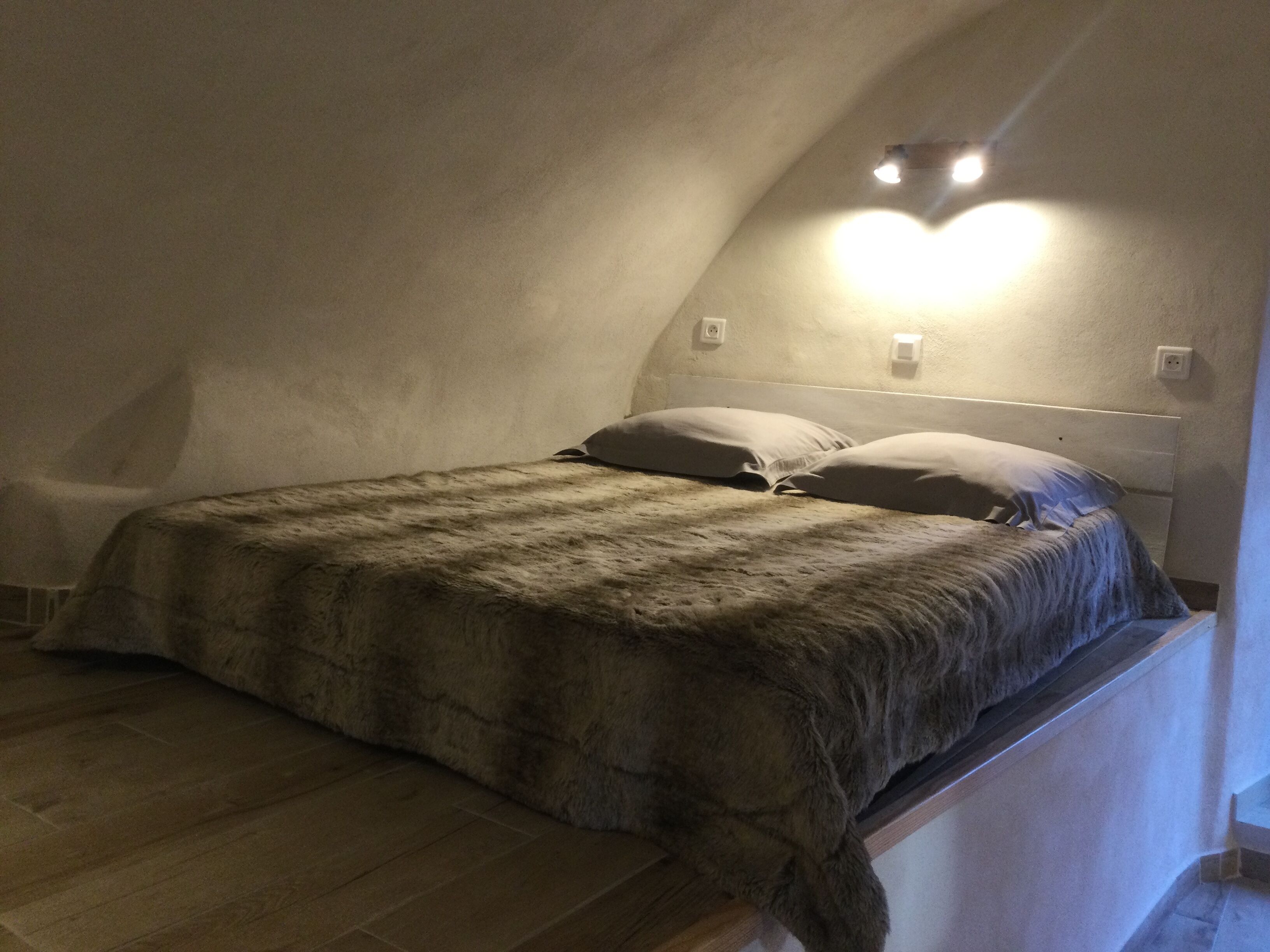 A bedroom with a sloped ceiling, a bed with a fluffy blanket, and a wall-mounted light fixture.