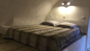 A bedroom with a sloped ceiling, a bed with a fluffy blanket, and a wall-mounted light fixture.