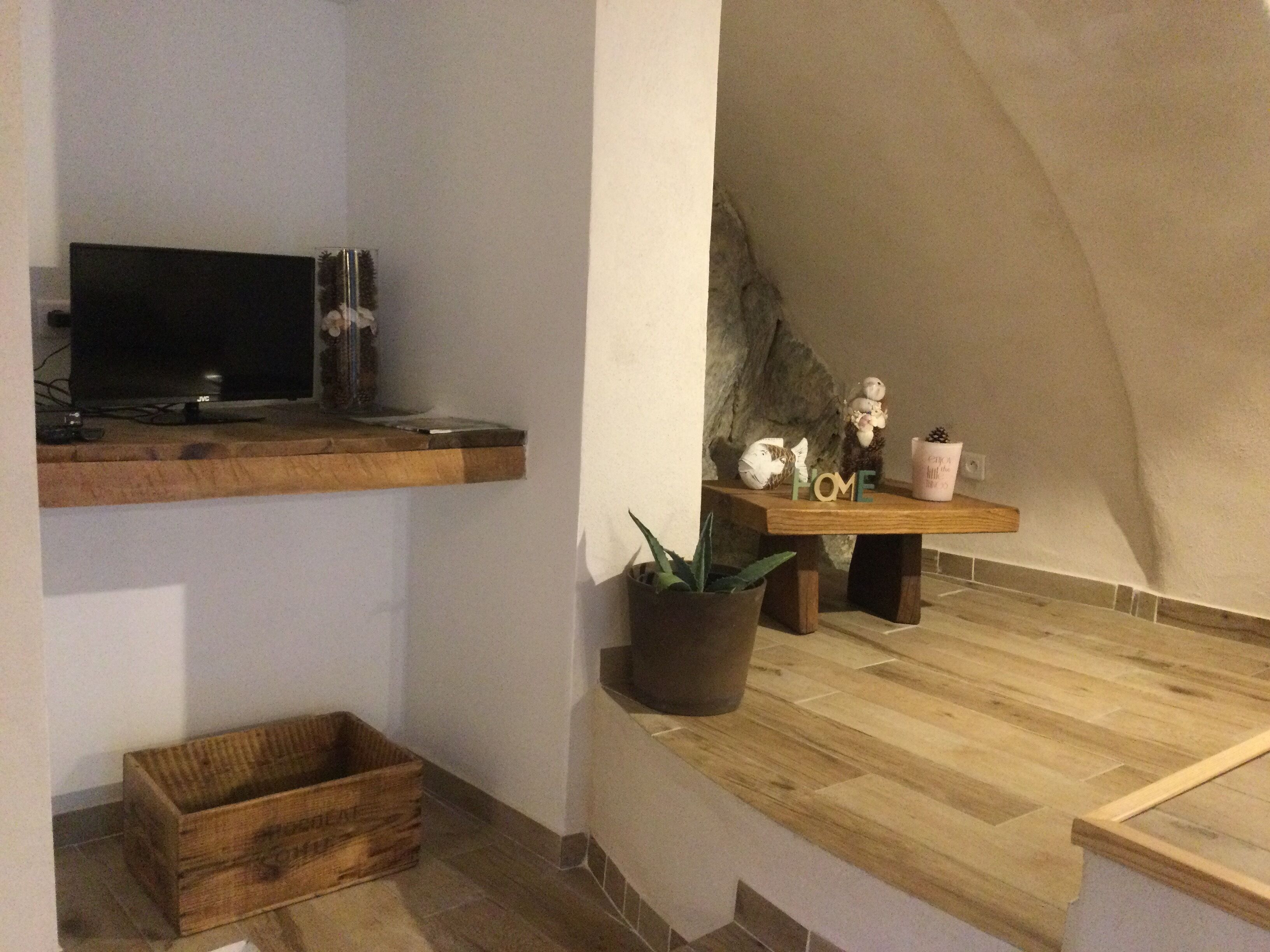A cozy room with a wooden TV stand, a small shelf with decorative items, a potted plant, and a wooden bench.