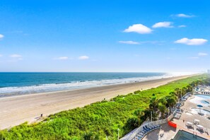 Un resort frente al mar con una extensa playa de arena, una zona de piscina y abundante vegetación.