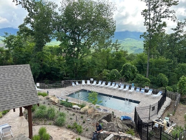 A rectangular pool with lounge chairs around it, surrounded by a stone deck and a wooden fence. - Make Hallmark Memories! Cozy mountain cabin in the woods.  (Gatlinburg)