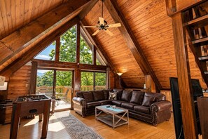 Un loft spacieux avec de hauts plafonds, de grandes fenêtres, un canapé en cuir, une table basse et une table de baby-foot.