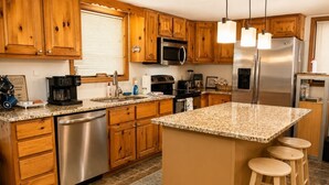 A kitchen with wooden cabinets, stainless steel appliances, a granite countertop, and a bar stool area.