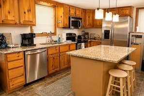 A kitchen with wooden cabinets, stainless steel appliances, a granite countertop, and a bar stool area.