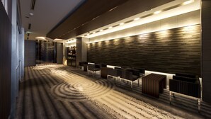 A modern hotel lobby with a curved carpet design, seating area, and a wall with a wood-like texture. - Village Kyoto (Kyoto)