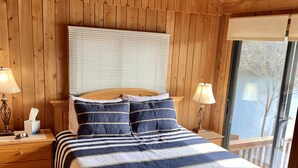A wooden-paneled bedroom with a large bed, two bedside tables, and a ceiling fan. - Cabin 2 at Cedar Key - Serene waterfront setting/No wake cove/Dog friendly! (Huddleston)