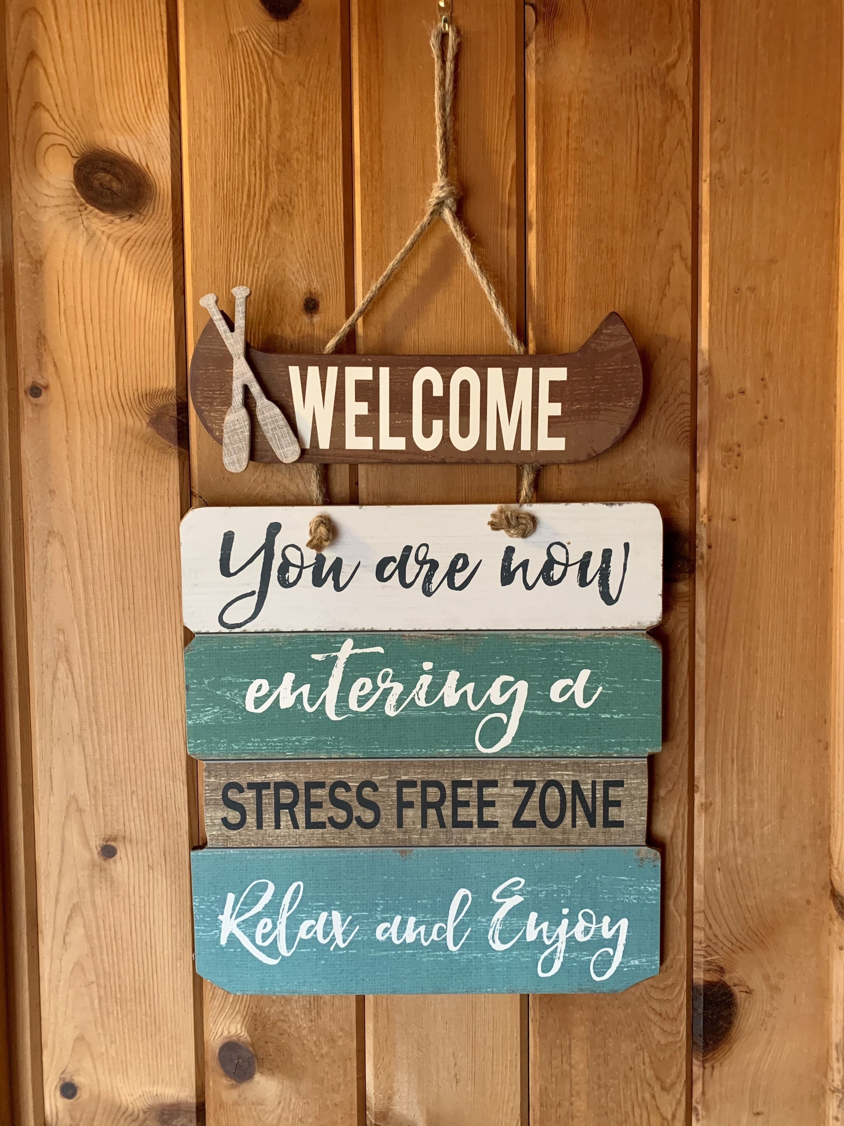 Un letrero de madera con las palabras 'WELCOME' y 'Ahora entras en una ZONA LIBRE DE ESTRÉS. Relájate y disfruta' sobre un fondo de madera rústica.