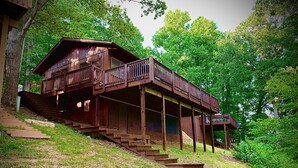 A wooden cabin with a balcony, surrounded by trees and a grassy area. - Cabin 2 at Cedar Key - Serene waterfront setting/No wake cove/Dog friendly! (Huddleston)