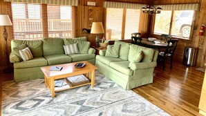 A cozy living room with a green sofa set, a wooden coffee table, and a dining table with chairs. - Cabin 2 at Cedar Key - Serene waterfront setting/No wake cove/Dog friendly! (Huddleston)