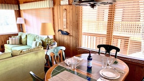A cozy dining area with a wooden table set for two, surrounded by wooden walls and a window with blinds. - Cabin 2 at Cedar Key - Serene waterfront setting/No wake cove/Dog friendly! (Huddleston)