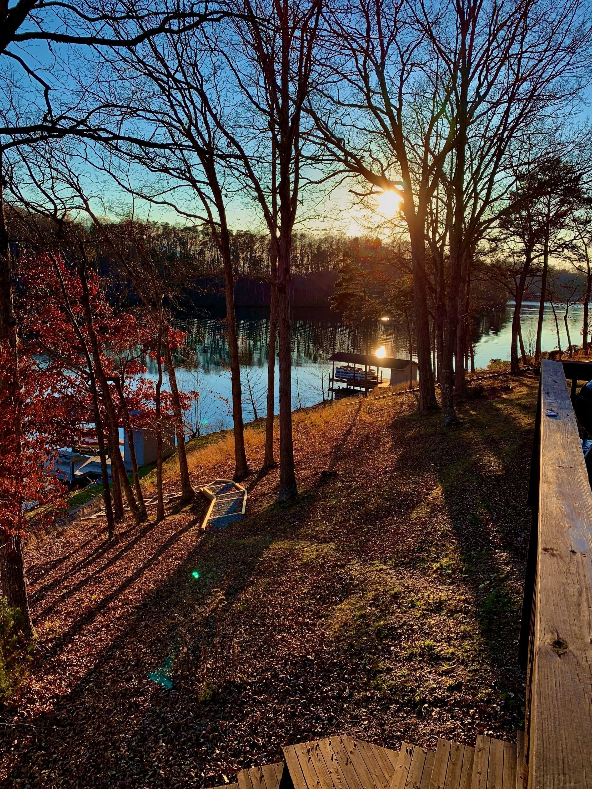 A lakeside view with a wooden deck, trees, and a dock extending into the water.