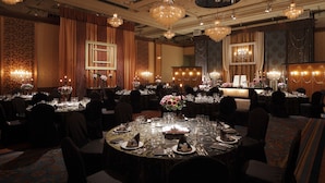 Une salle à manger formelle, avec plusieurs tables rondes dressées pour un repas, de grands lustres et des décorations murales élégantes.