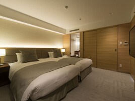 A hotel room with a large bed, two bedside tables, a nightstand, a wall-mounted TV, and a wooden wardrobe.