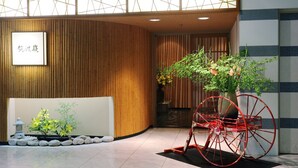 Un espace d’accueil avec un mur en bois, une enseigne avec des caractères chinois, une roue décorative rouge et un petit jardin agrémenté de rochers et de plantes.