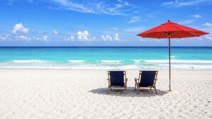 A beach with two chairs and a red umbrella.