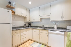 A kitchen with white cabinets, a granite countertop, a dishwasher, and a coffee maker.