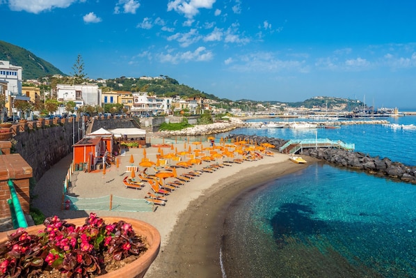 A coastal town with a beach, clear blue water, and buildings in the background.