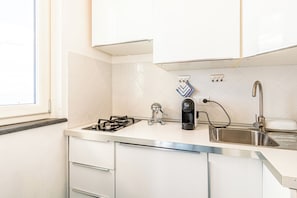 Een moderne keuken met witte kastjes, een roestvrijstalen spoelbak, een gasfornuis en een koffiezetapparaat.