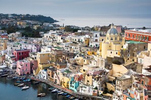 A densely packed coastal town with colorful buildings, a prominent church with a dome, and boats docked along the waterfront.